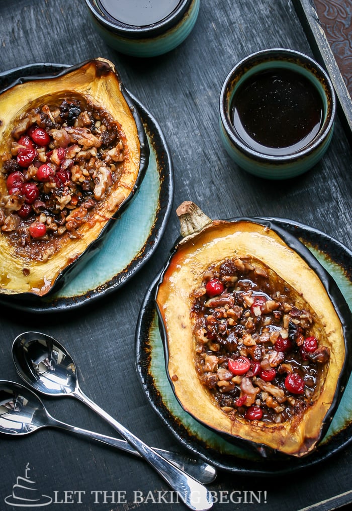 Acorn squash filled with walnuts and cranberries on a plate with spoons.
