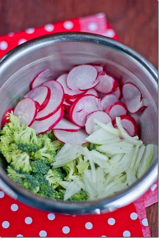 Radishes, broccoli, and onions in a bowl on a red polka dot napkin.