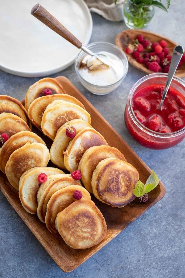 A plate with Russian pancakes, surrounded by jam and sour cream topping for them.
