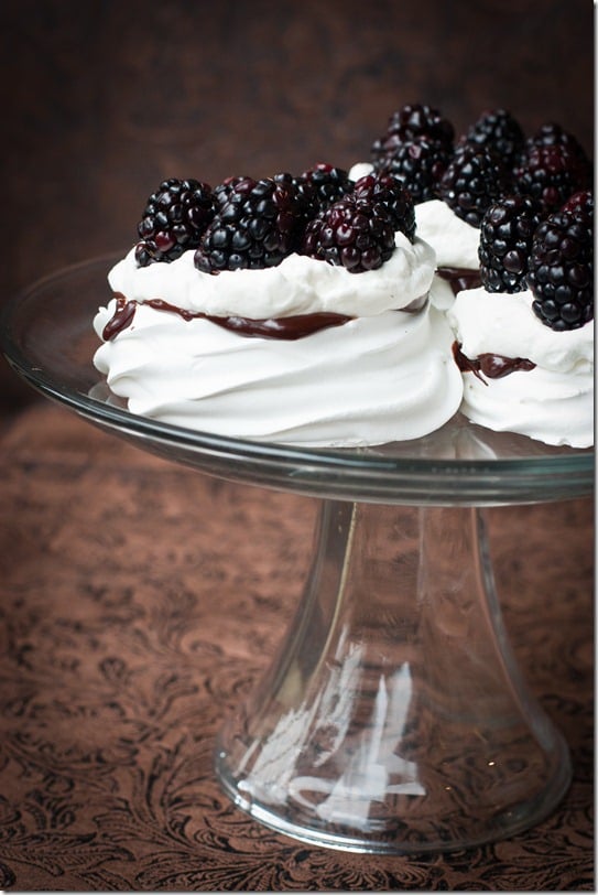 Classic meringue recipe filled with chocolate topped with blackberries on a glass cake platter. 
