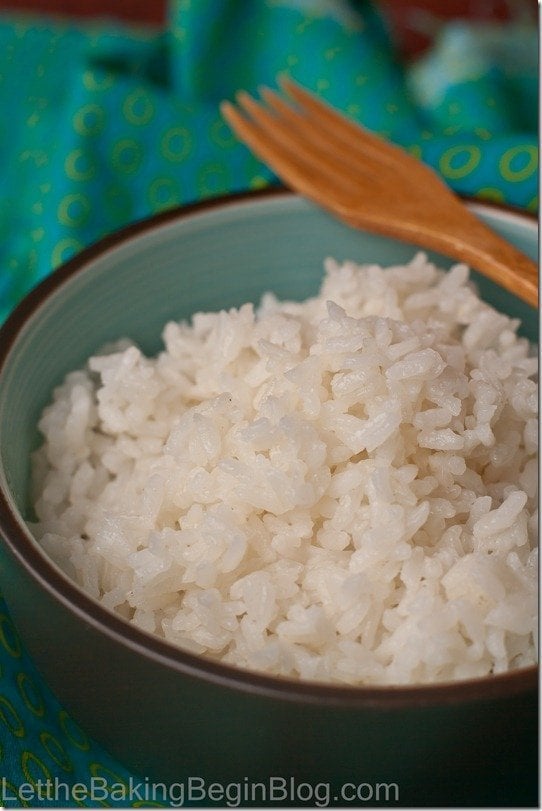 Rice in a decorative blue and black bowl with a wooden fork on a blue napkin.