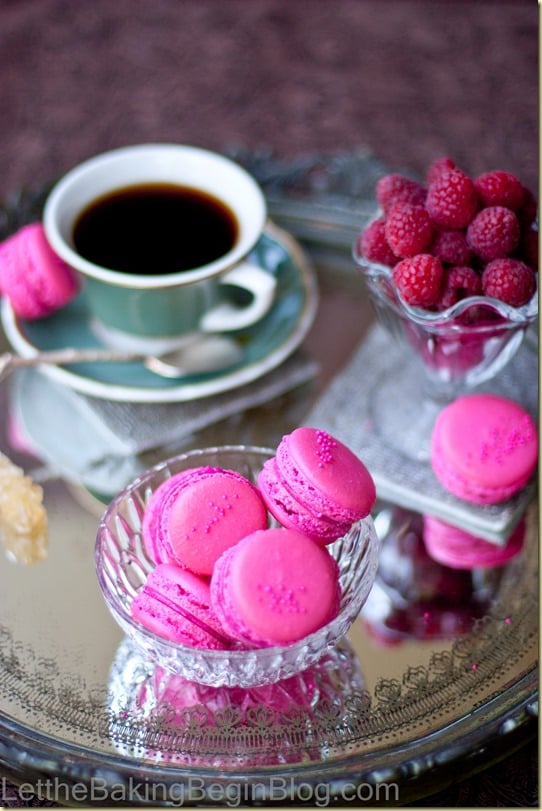 Raspberry scones in a glass bowl on a metal platter next to a cup of coffee. 
