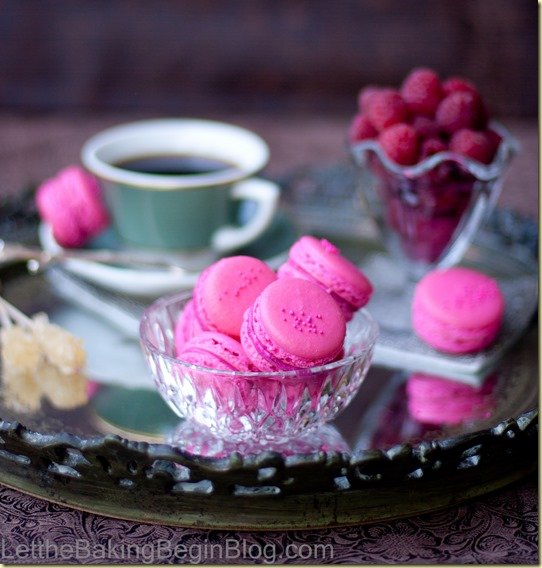 Raspberry Macarons in a glass bowl in a tray with raspberries and coffee. 