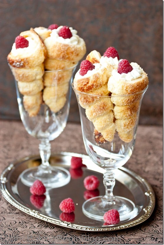 Six cream horns in two different glass cups on a silver platter.