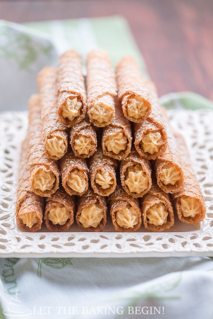 A stack of crispy wafers sprinkled with powdered sugar on a white decorative tray. 
