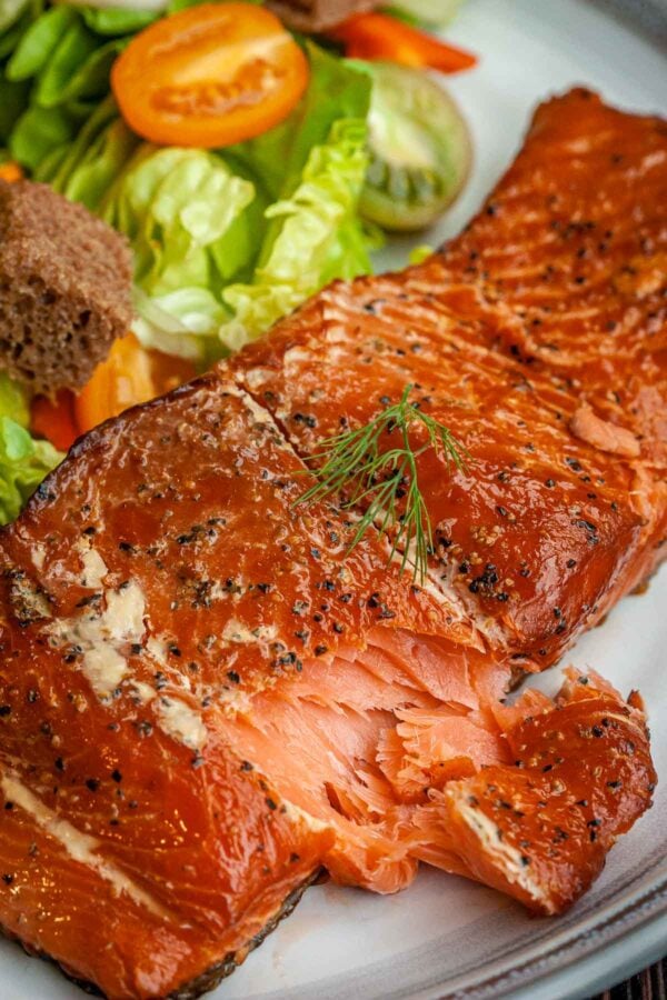 Smoked salmon fillet on a plate with seasonings, next to a mixed salad. 
