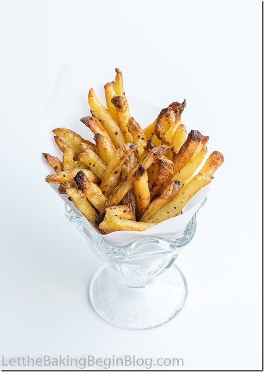 French fries topped with ground pepper in a cup with parchment paper. 