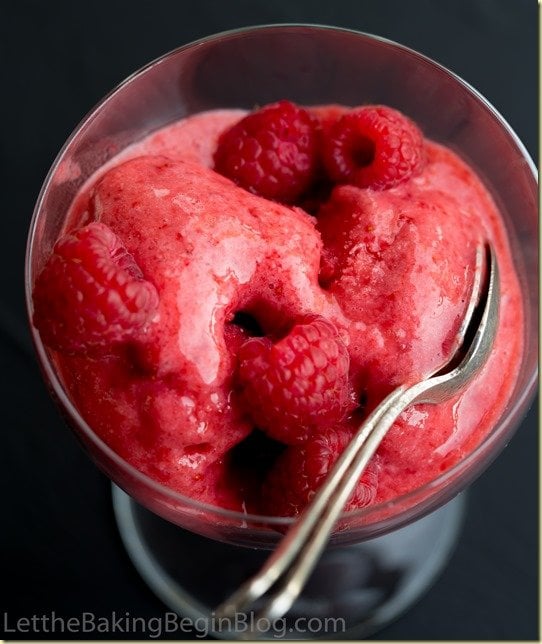 Strawberry sorbet with fresh raspberries in a glass cup and a spoon.