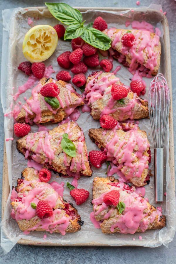 A baking pan full of raspberry scones, drizzled with raspberry glaze and raspberries scattered throughout.