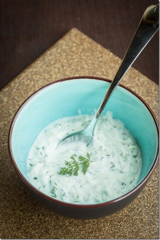 Tzatziki sauce in a decorative bowl topped with fresh greens and a spoon.