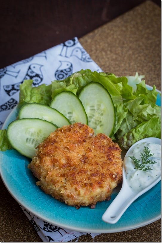 Salmon cake with tzatziki sauce on a decorative plate with cucumbers and romaine. 