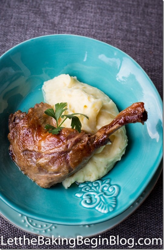 Duck sided with mashed potatoes topped with fresh greens on a blue decorative plate.