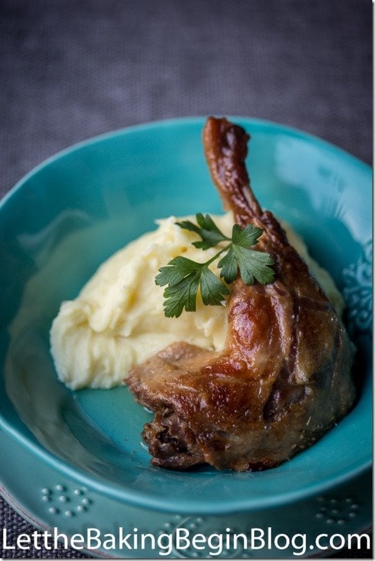 Baked Duck Confit next to mashed potatoes with parsley leaf on top on a turquoise plate.