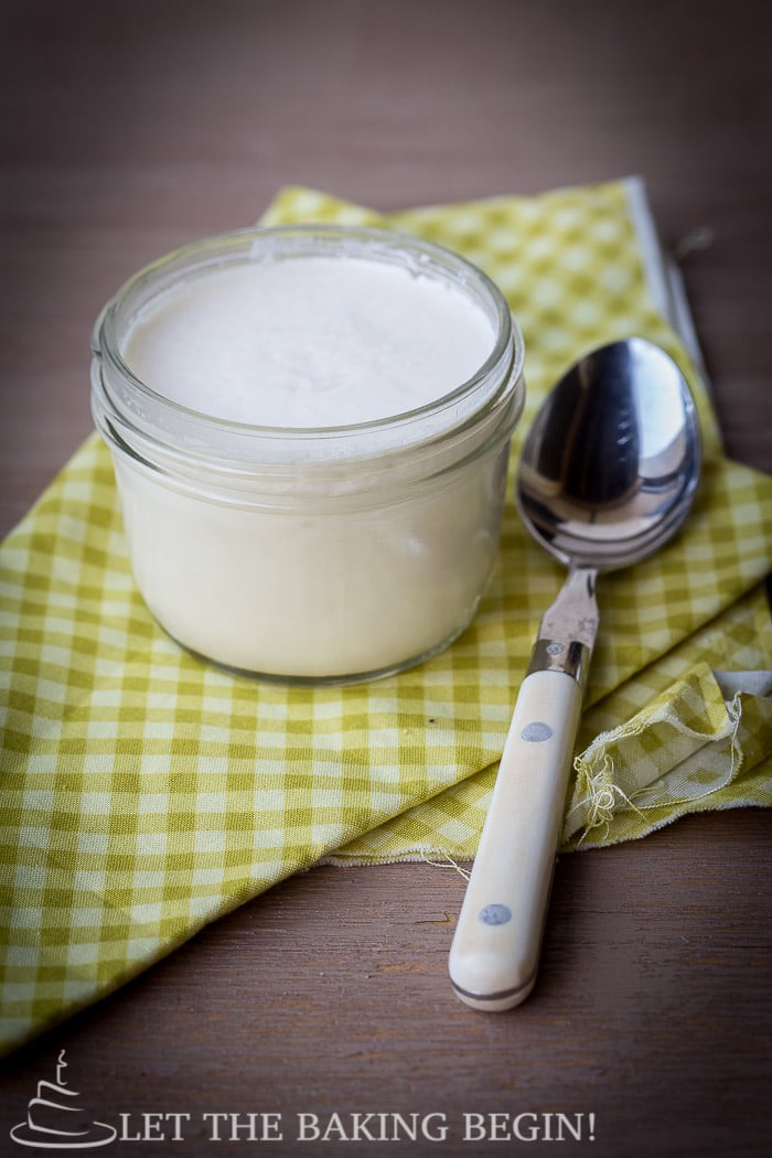  Side view of homemade yogurt in a mini mason jar with a spoon under a green checkered napkin.
