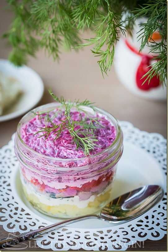 Layered beet salad topped with fresh greens in a mini mason jar on a white decorative plate.