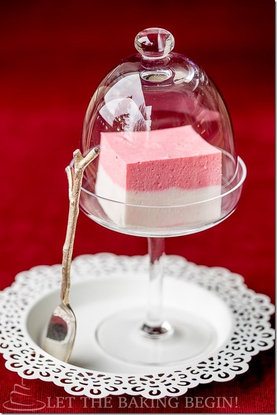 Strawberry jello in a glass with cover on a white decorative plate with a wooden spoon.