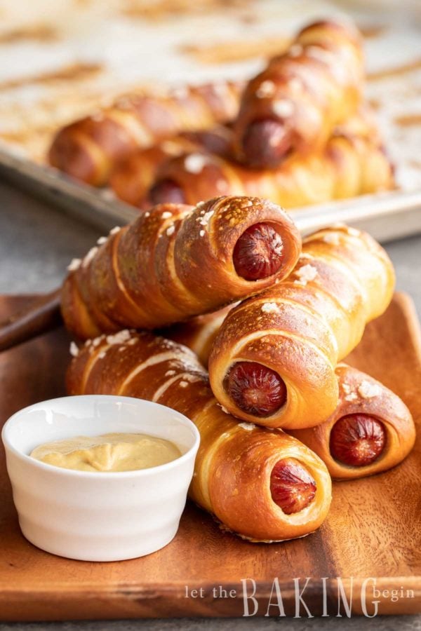 Pretzel dogs piled onto a plate with a side of mustard.