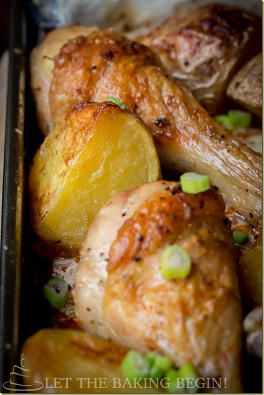 Up close picture of a chicken drumstick and potatoes in a baking sheet.