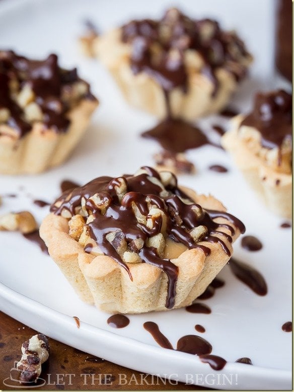 Tartlets with walnuts and topped with chocolate on a white tray.