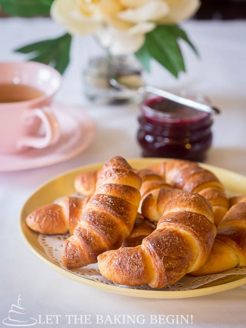 Crescents on a yellow decorative plate with jam and tea on a table.