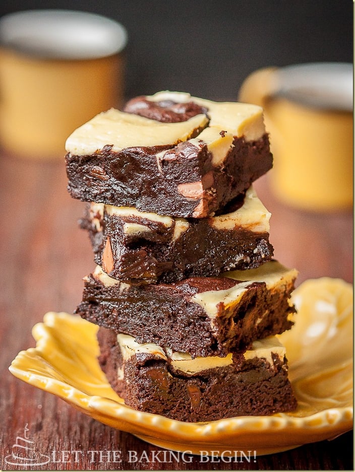 Cheesecake brownies with moist chocolate and swirls of sweet cheesecake stacked on top of each other on a yellow plate.