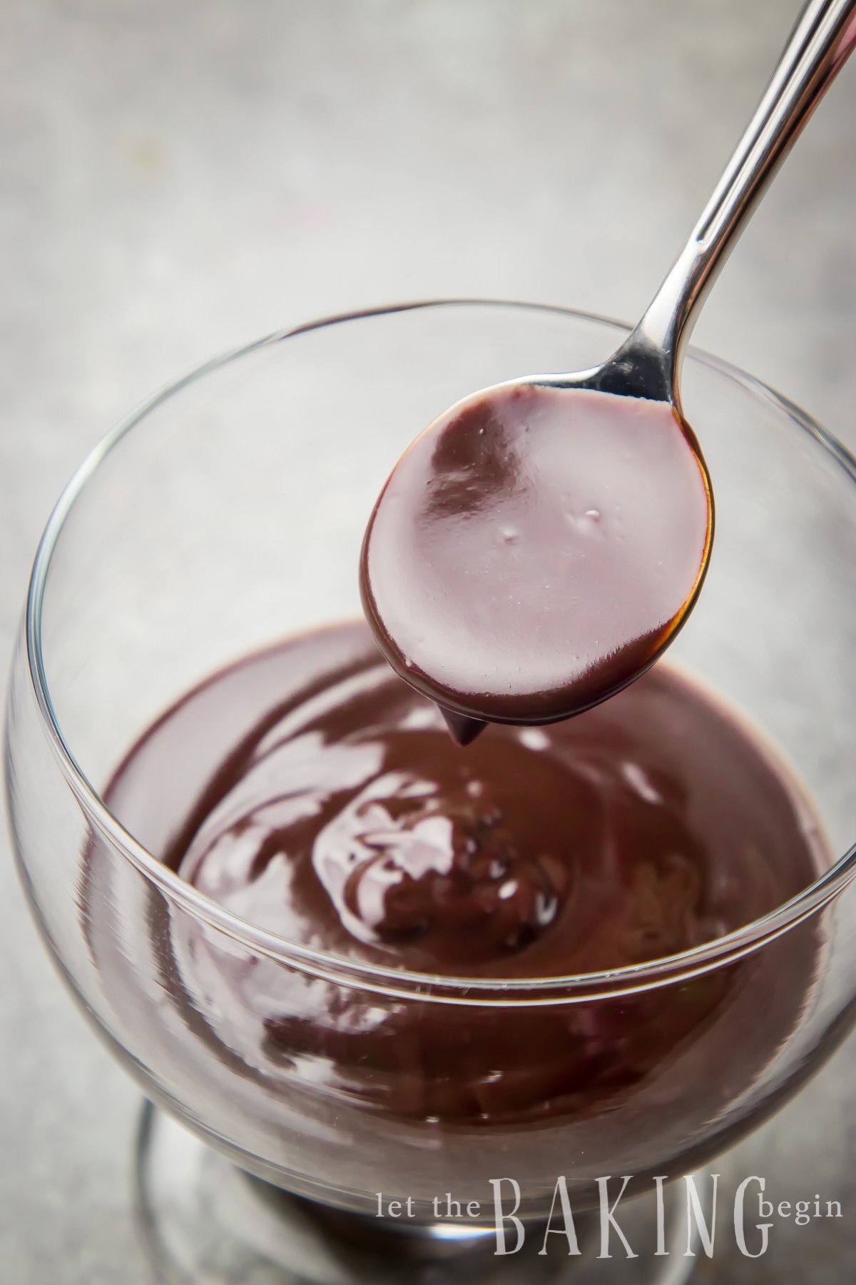 Extra shiny chocolate ganache in a glass cup with a spoonful of chocolate. 