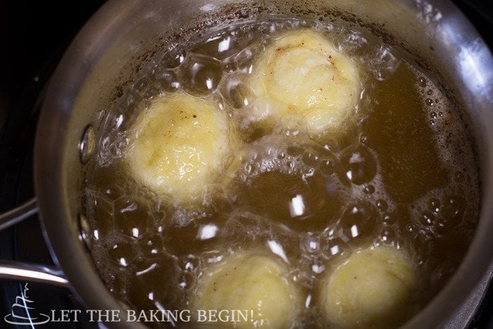 Four donuts being fried in a pot of oil.
