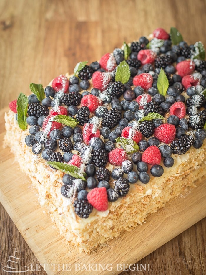 Full cake topped with raspberries, blueberries, blackberries, mint, and powdered sugar on a wooden cutting board. 
