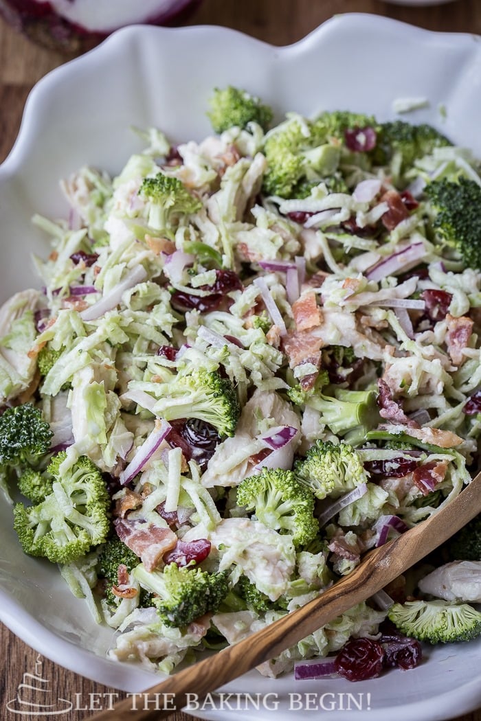 Mixed broccoli salad in a white bowl with a wooden spoon.