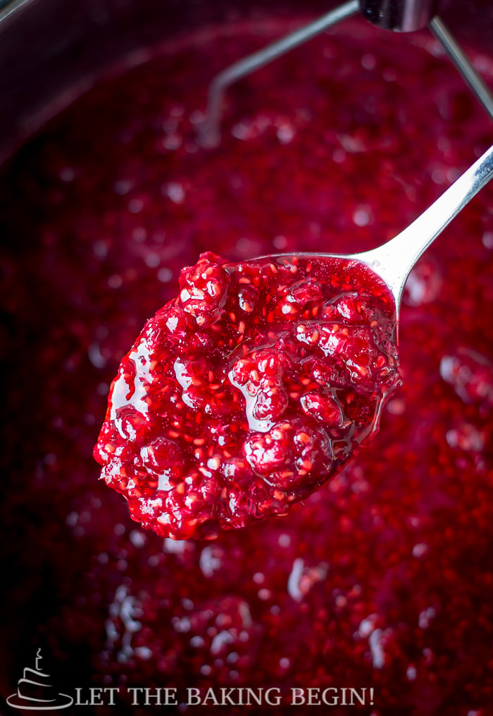Sweet raspberry jam in a pot with a spoonful of raspberry jam. 