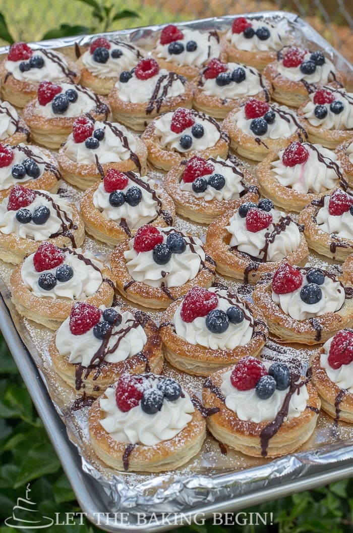 Puff pastry berries and cream tarts on a baking sheet sprinkled with powdered sugar and chocolate drizzle. 