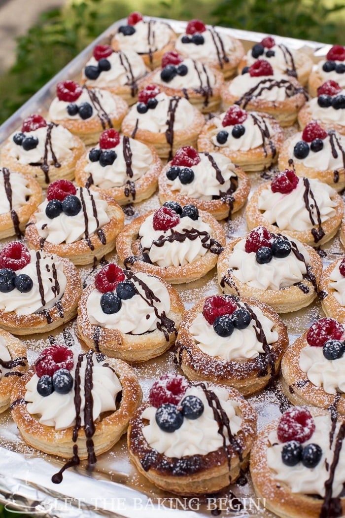 Puff pastry tarts filled with chocolate ganache, sweet cream and berries on a baking sheet, topped with powdered sugar. 