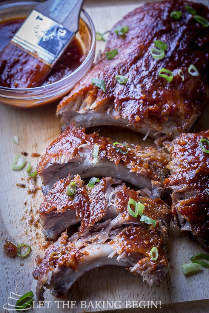 Cut ribs on a wooden cutting board topped with fresh greens and barbecue sauce.