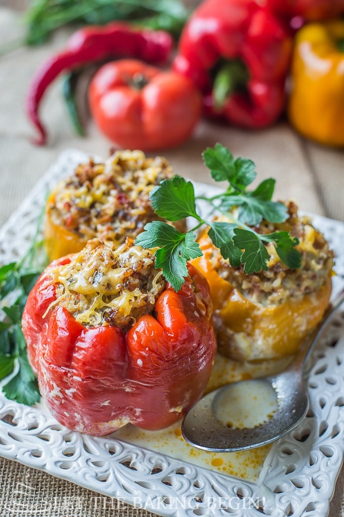 Three stuffed peppers, two yellow peppers and one red peppers, topped with fresh greens in a white decorative plate.