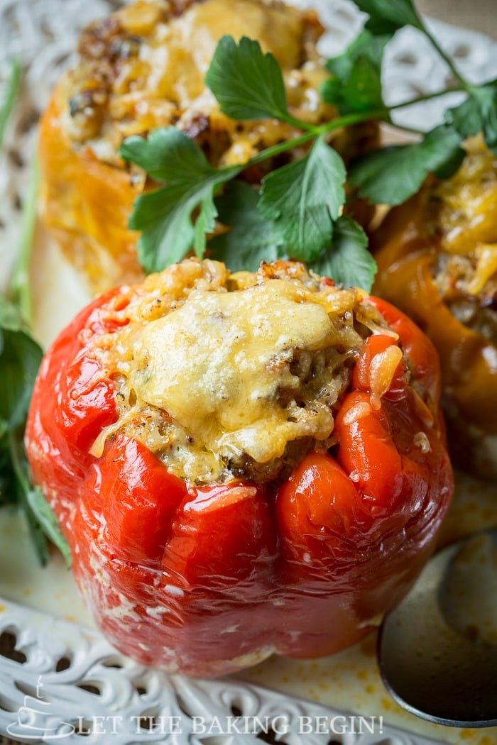  Top view of stuffed red peppers topped with melted cheese on a white decorative plate.