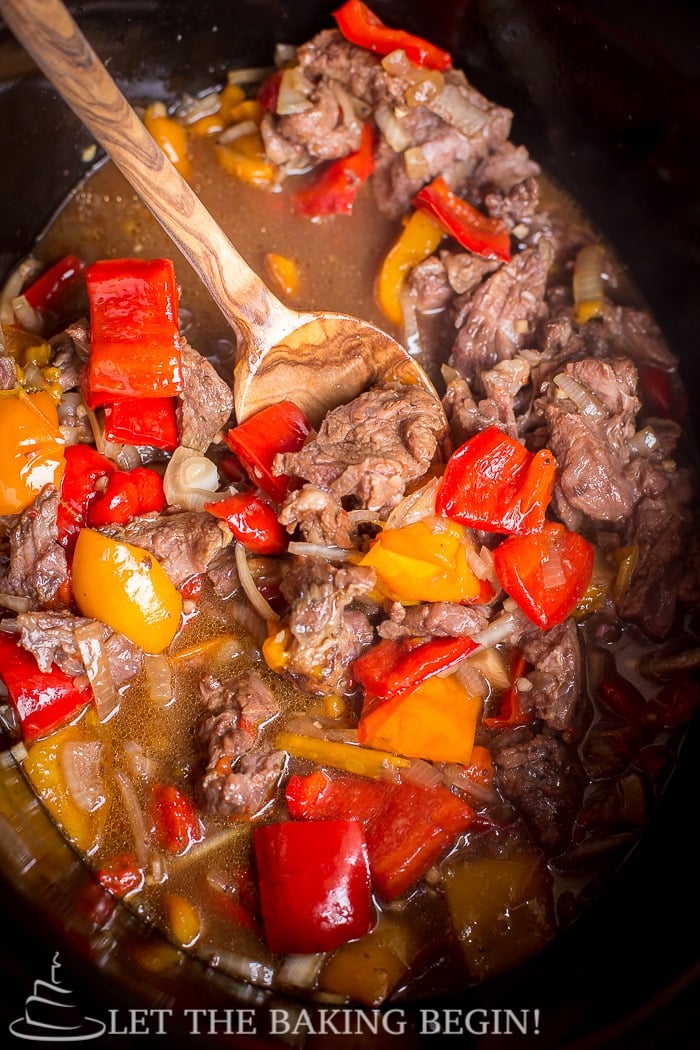 Spicy Slow Cooker Beef & Bell Pepper in a crock pot with sauce, and a wooden spoon. A simple recipe for beef recipes! 