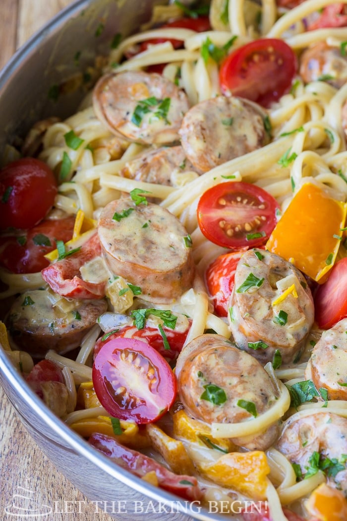 Sausage pepper fettuccine in a skillet with parsley and tomatoes. 