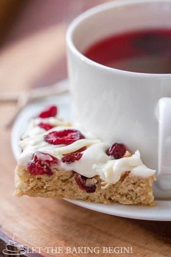 Cranberry bliss bar on a white decorative plate with a cup of tea in a white mug.