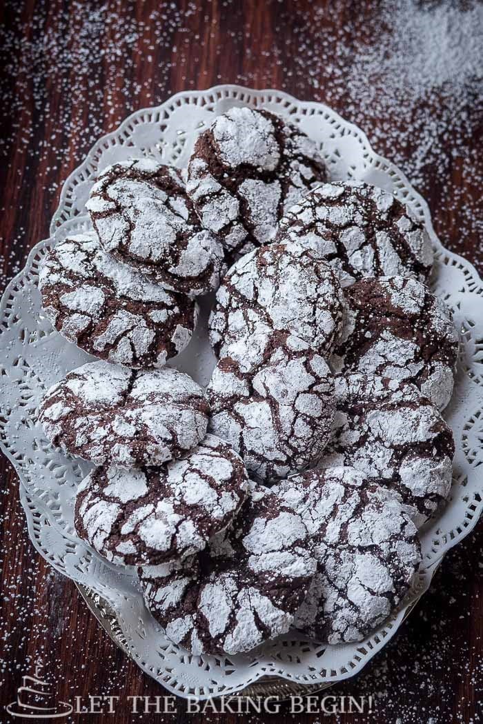 Top view of chocolate crinkle cookies on a decorative plate topped with powdered sugar.