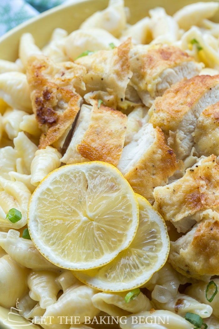 Close up picture of fried chicken on top of garlic pasta with fresh lemon slices.