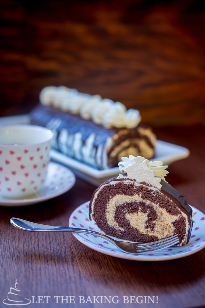 Slice of chocolate roll with walnuts topped with chocolate and chantilly cream on a decorative plate.