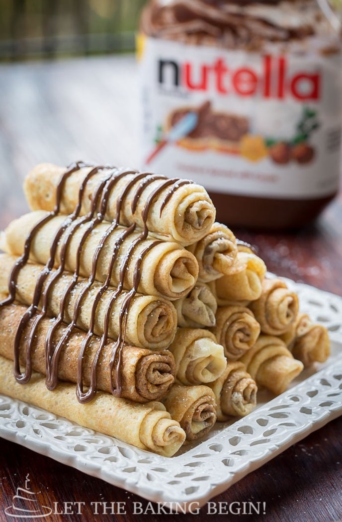 Folded crepes on a white decorative plate topped with Nutella.