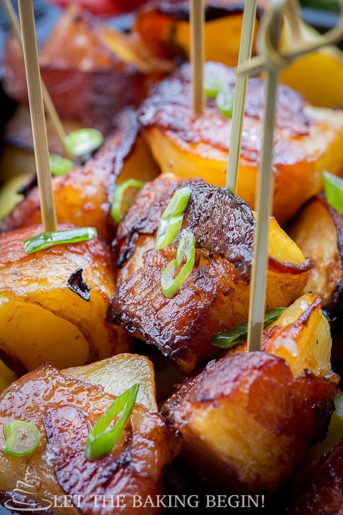 Bacon wrapped potatoes on toothpicks topped with chopped greens. 