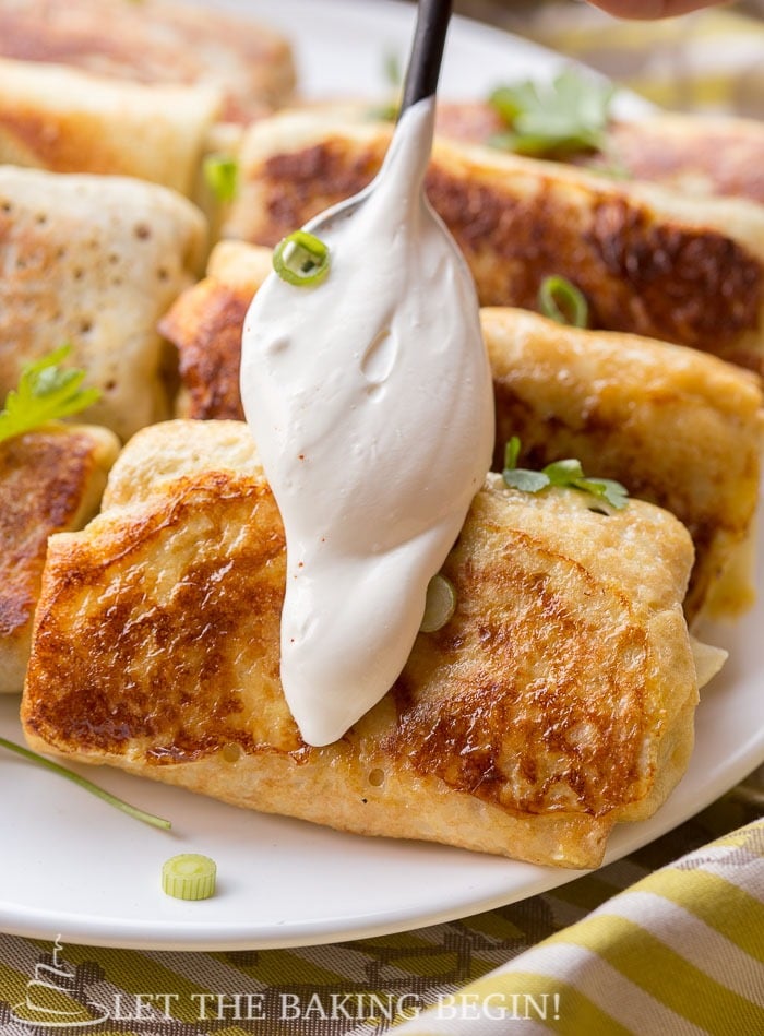 Crepes on a white decorative plate topped with fresh greens and a dollop of sour cream. 