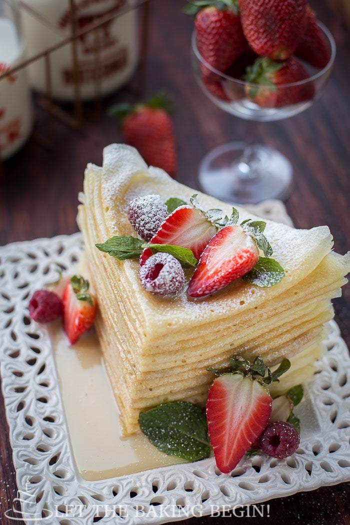Folded crepes on a white plate topped with berries and sprinkled with powdered sugar. 
