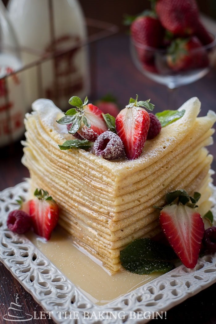 Buttermilk crepes stacked on top of each other topped with fresh strawberries and raspberries. 