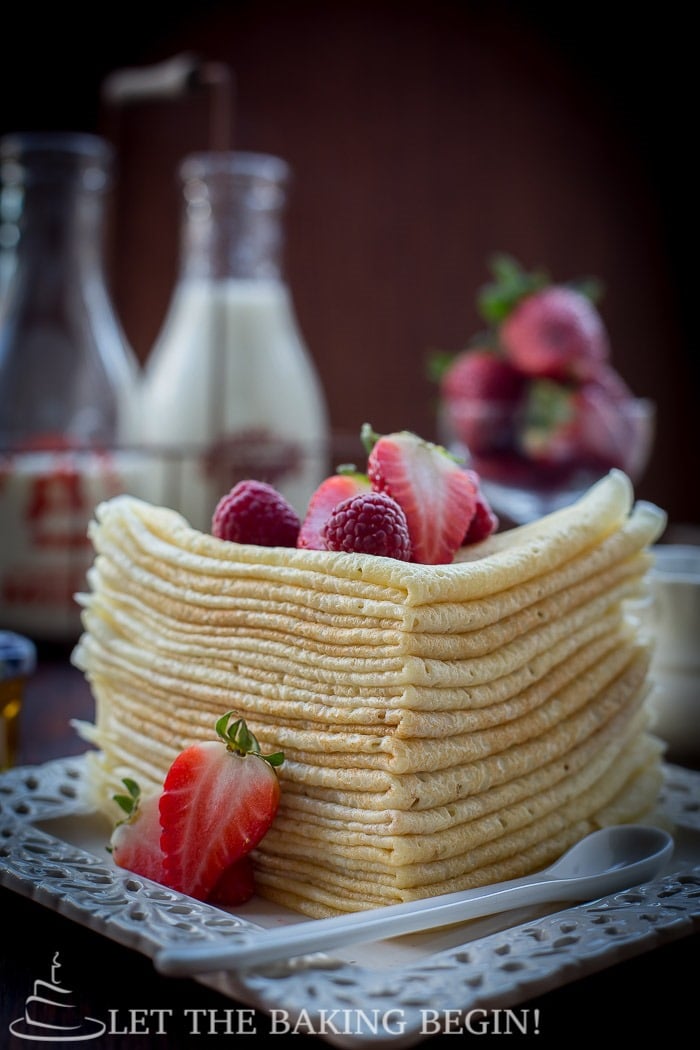 Choux pastry crepes folded and stacked on top of each other on a white plate topped with fresh berries. 