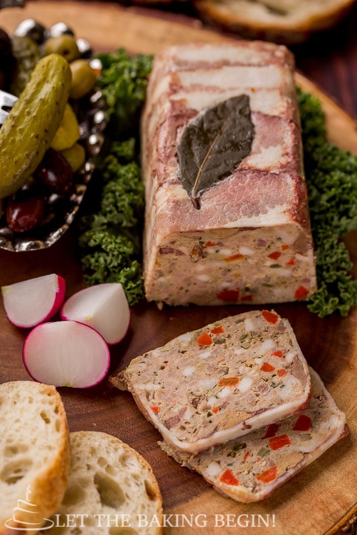 Country style pate on top of lettuce sided with radishes, slices of bread, olives and pickles on a wooden board.