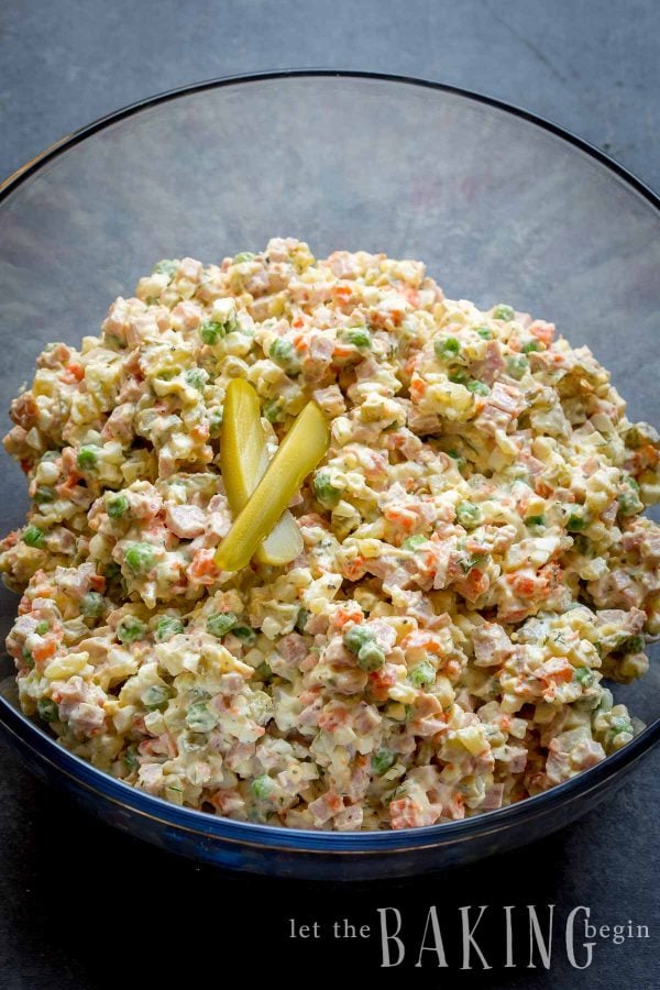 Russian potato salad in a glass bowl topped with pickles. 