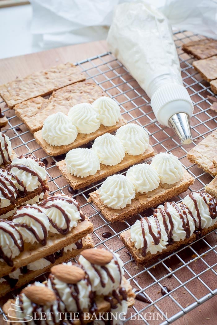 Puff pastry sheets topped with white chocolate mousse on a cooling rack. 